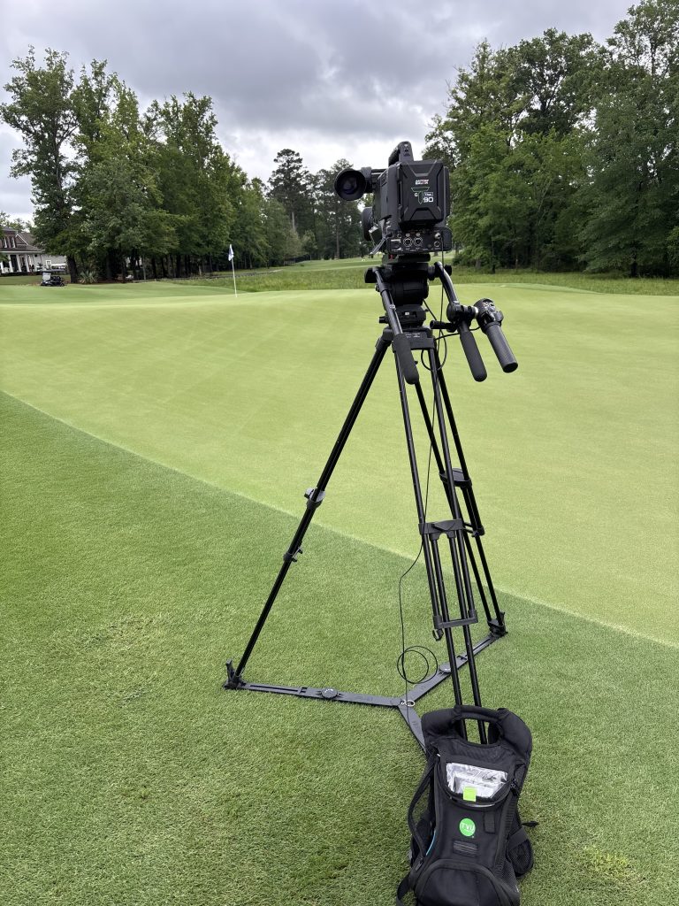 Broadcast camera on a tripod beside the green